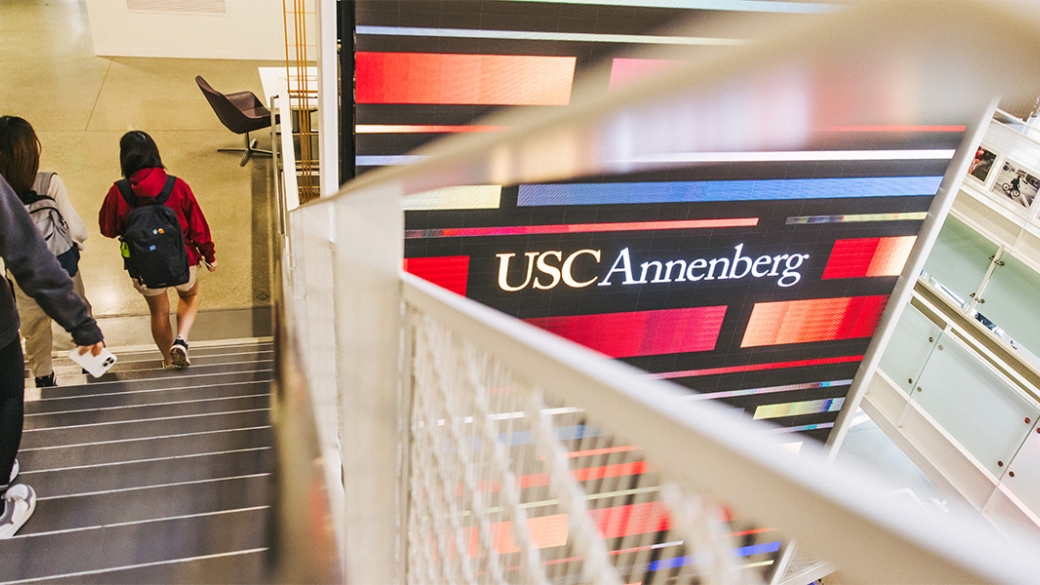 Students walking down a staircase while the Wallis Annenberg Hall Media Wall shines in the backgroud.