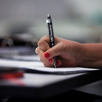 A shot of a hand with red nail polish writing on a piece of paper with a pen that says “USC Annenberg.”